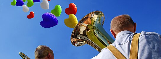 Blasmusiker spielen Musik und Luftballonherzen steigen zum Himmel.
