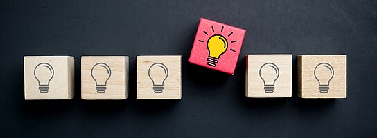 6 Holzklötzchen bedruckt mit schwarz-weißen Glückbirnen. Nur eine leuchtet in Farbe.